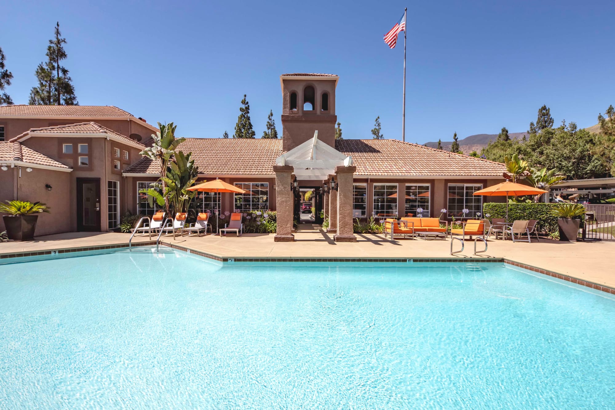 Resort-style swimming pool with lounge chairs and umbrellas at Sierra Del Oro Apartments in Corona, California