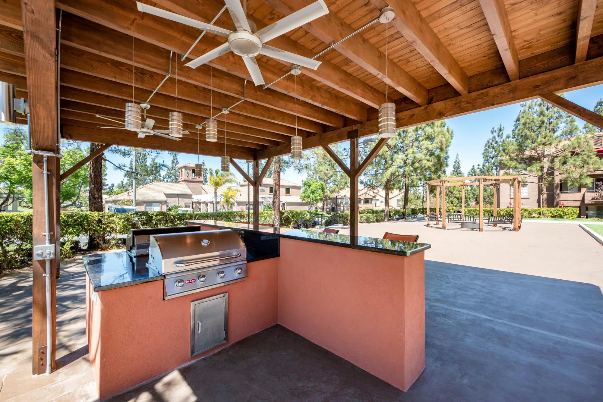 Covered BBQ area with bar top seating and fans at Sierra Del Oro Apartments in Corona, California