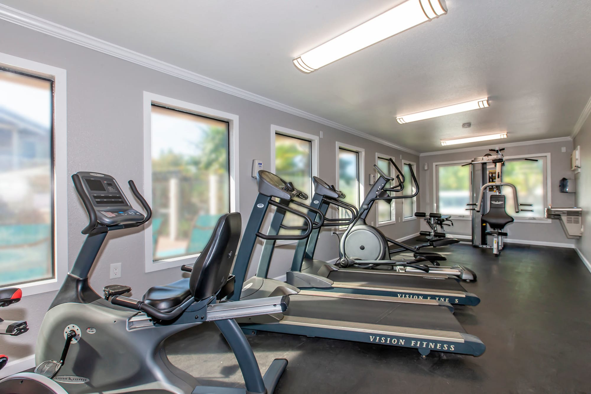 Fitness Center with cardio machines looking through large windows out to the pool area at Sommerset Apartments in Vacaville, CA