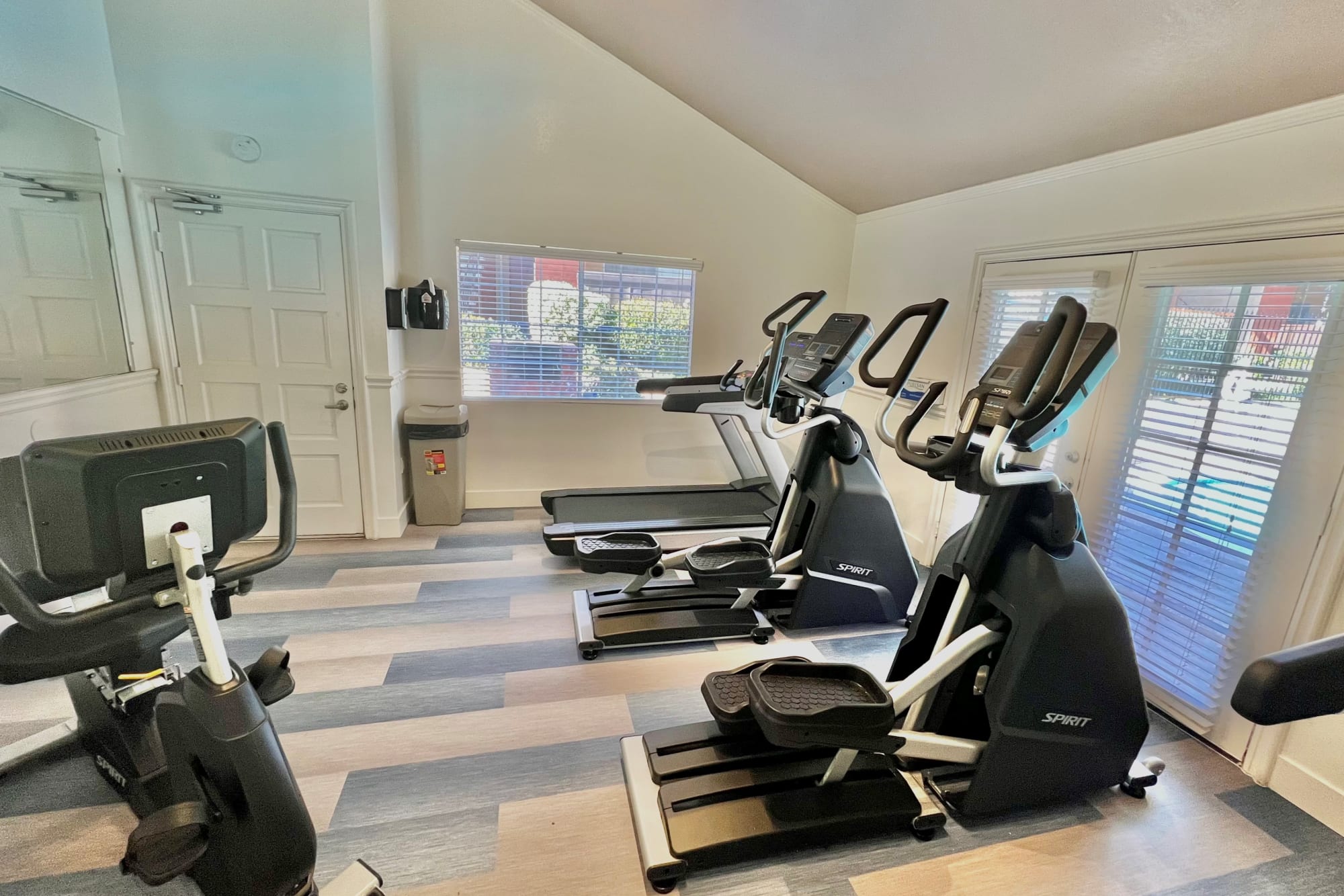 Fitness center with cardio machines looking through large windows to pool at Shadow Ridge Apartments in Oceanside, California