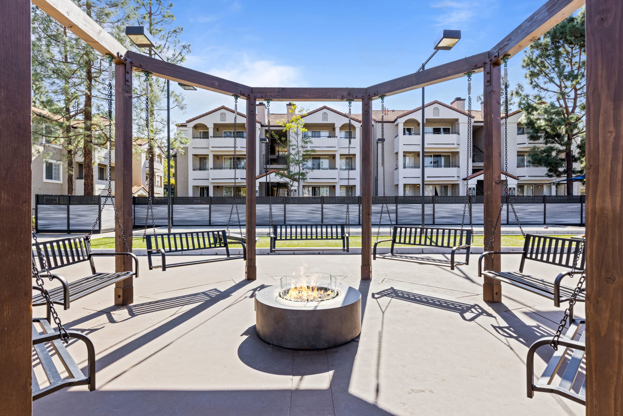 Fire pit surrounded by swing seating at Sierra Del Oro Apartments in Corona, California