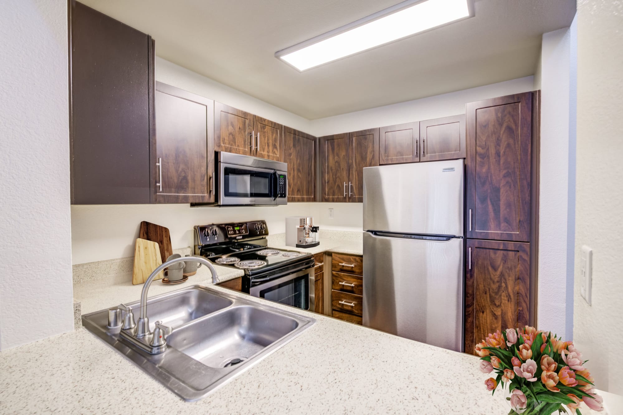 Renovated kitchen with brown cabinets and stainless steel appliances at Tuscany Village Apartments in Ontario, California