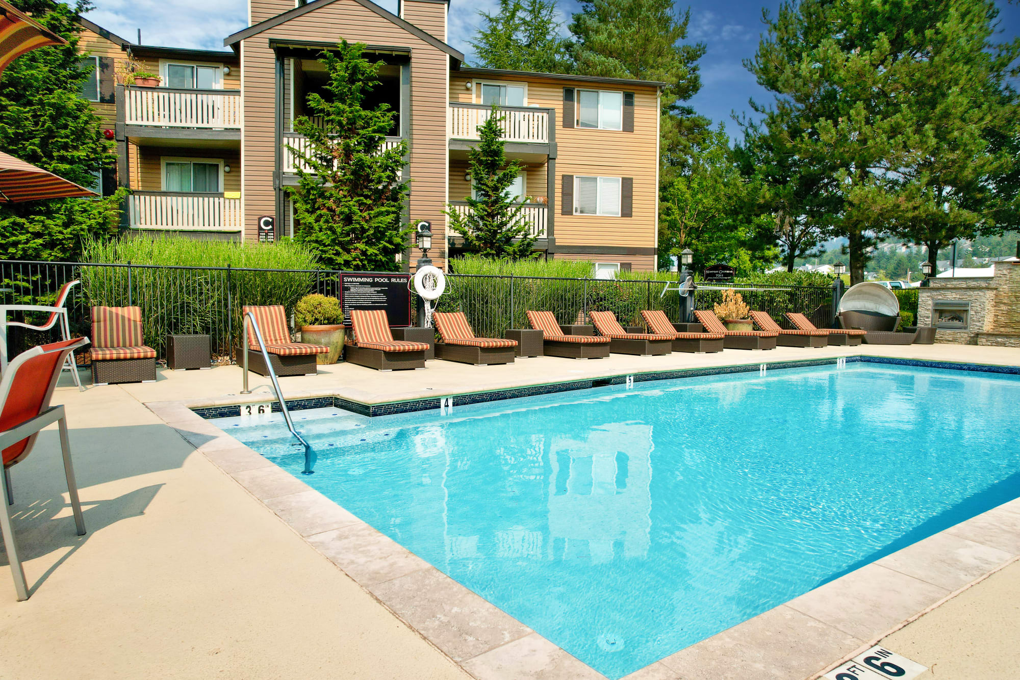 Sparking pool view with lounge chairs, tables and umbrellas at Newport Crossing Apartments in Newcastle, Washington