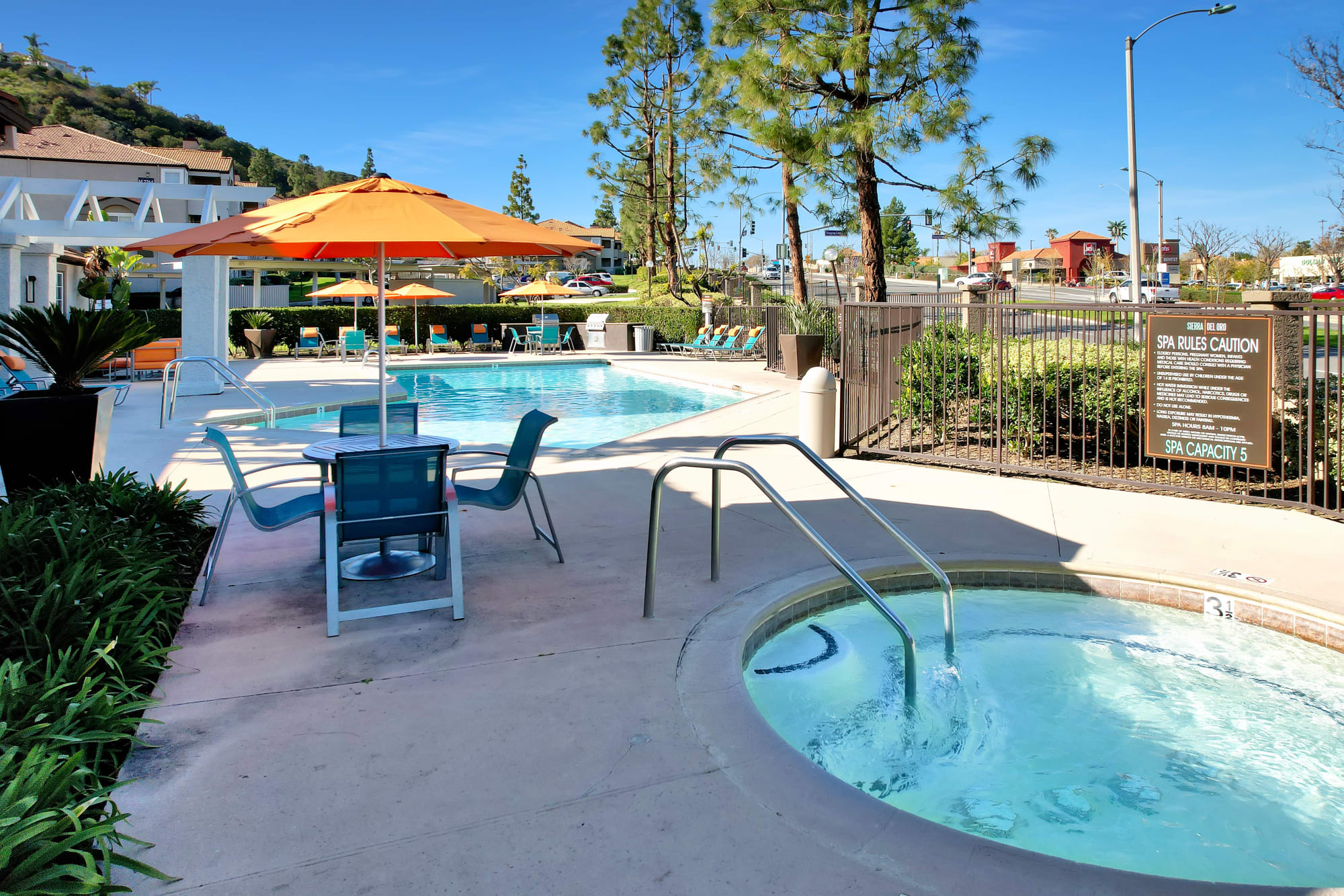 Pool with lounge chairs and umbrellas at Sierra Del Oro Apartments in Corona, California