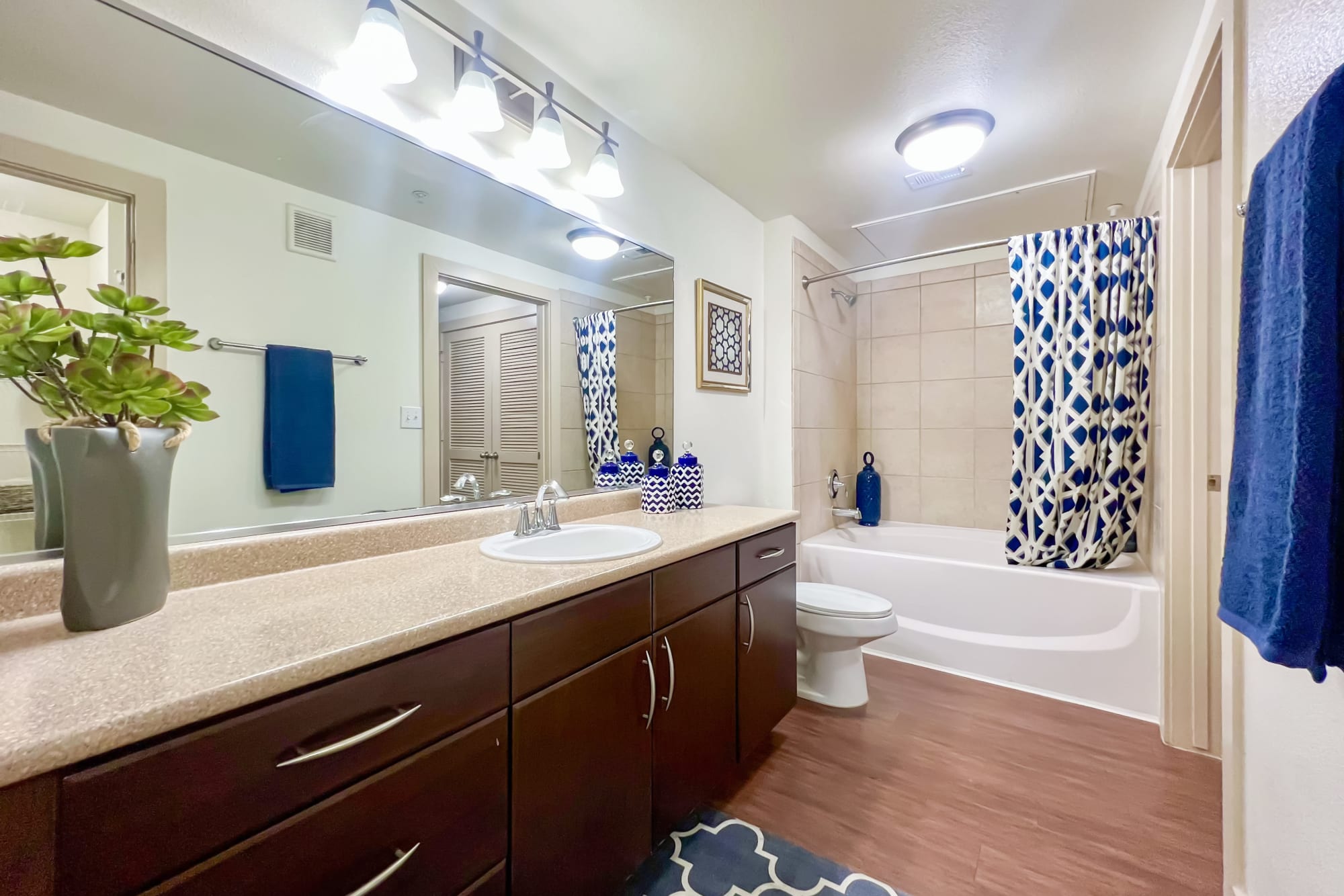 A renovated bathroom with brown cabinets, a large vanity and a mirrored closet door at Broadstone Grand Avenue in Pflugerville, Texas