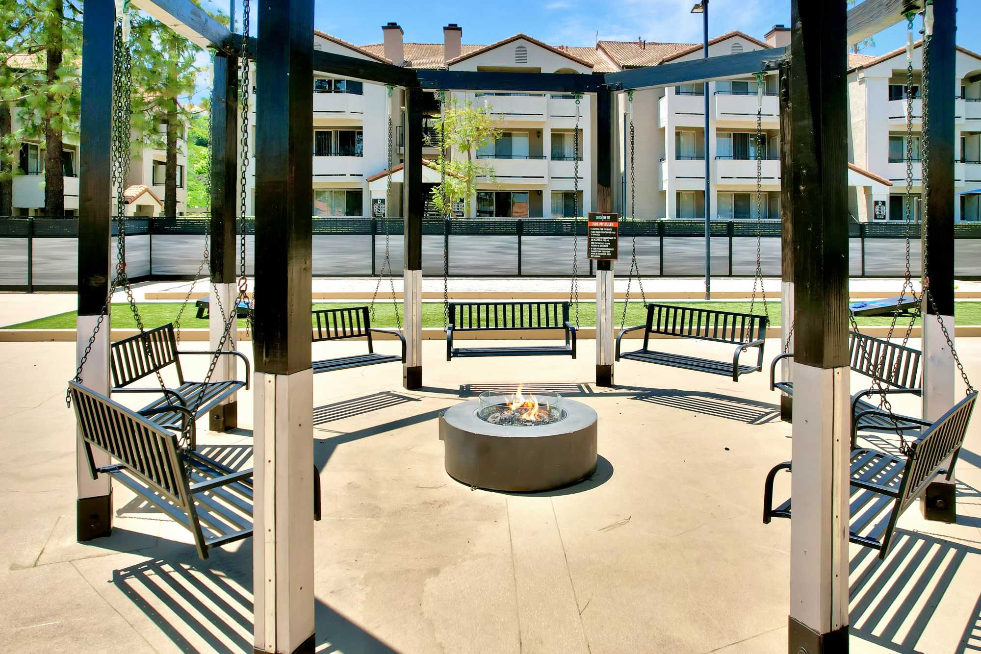 Fire pit surrounded by swing seating at Sierra Del Oro Apartments in Corona, California