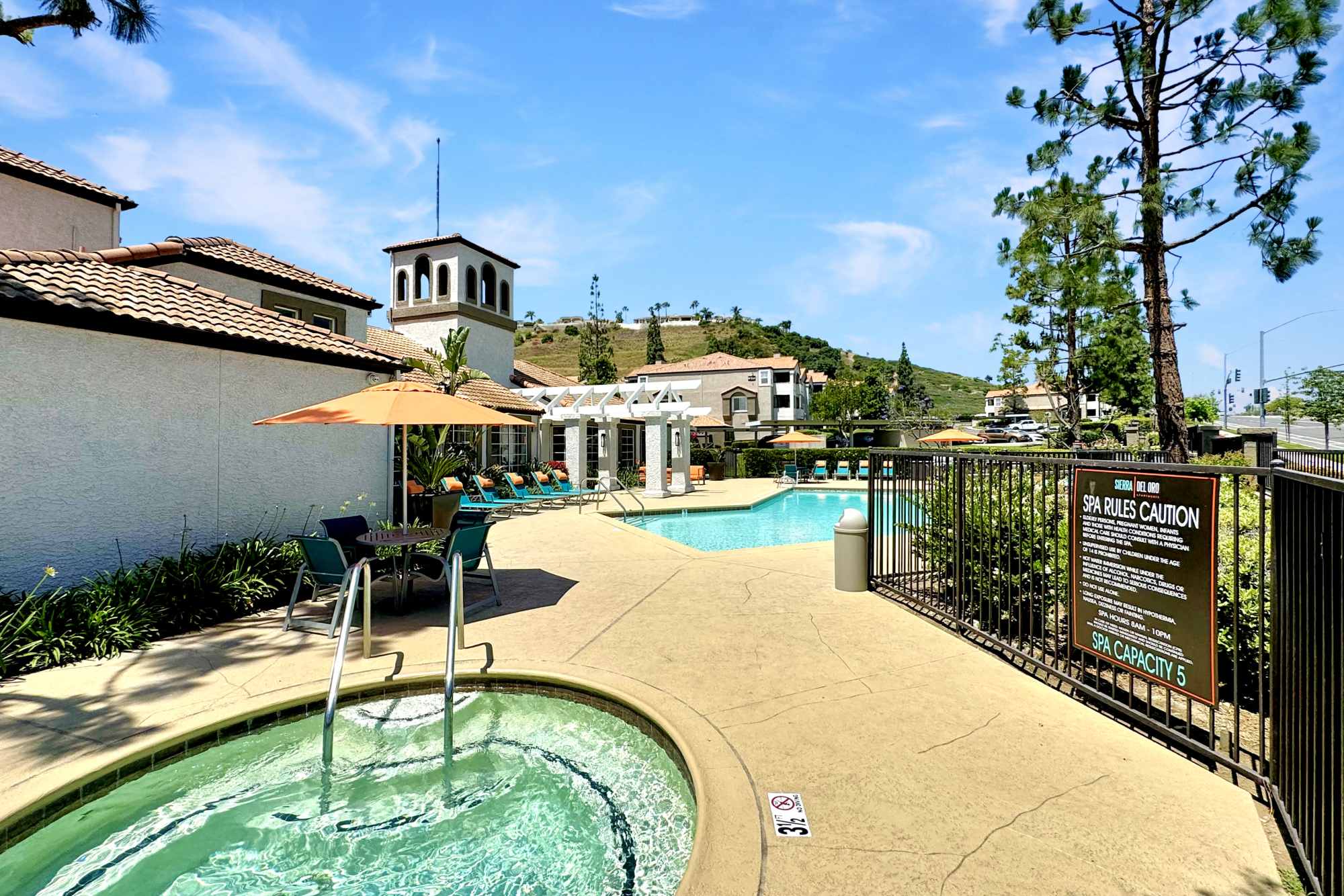 Pool with lounge chairs and umbrellas at Sierra Del Oro Apartments in Corona, California