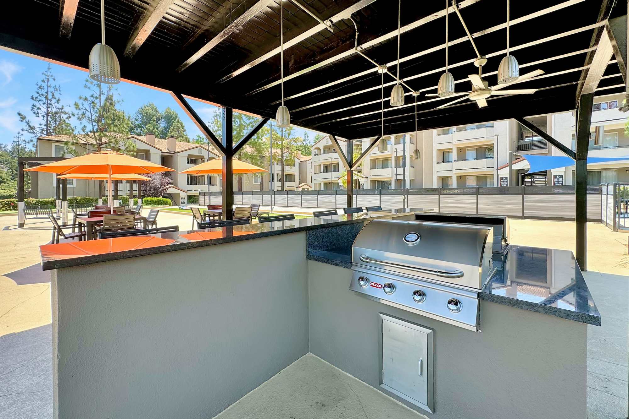 Covered BBQ area with bar top seating and fans at Sierra Del Oro Apartments in Corona, California