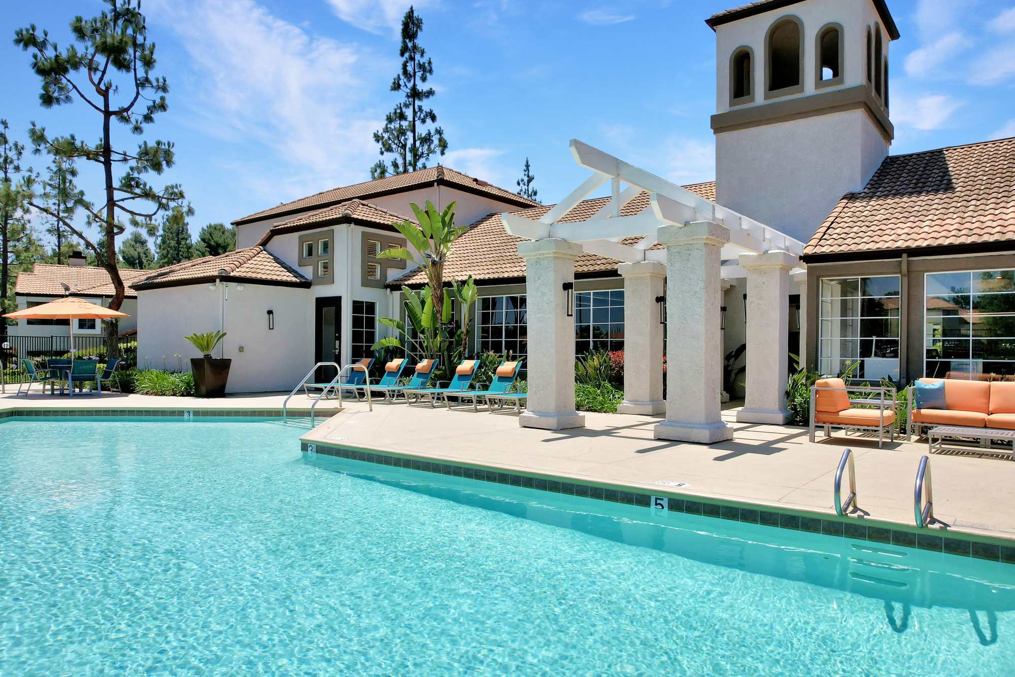 Resort-style swimming pool with lounge chairs and umbrellas at Sierra Del Oro Apartments in Corona, California