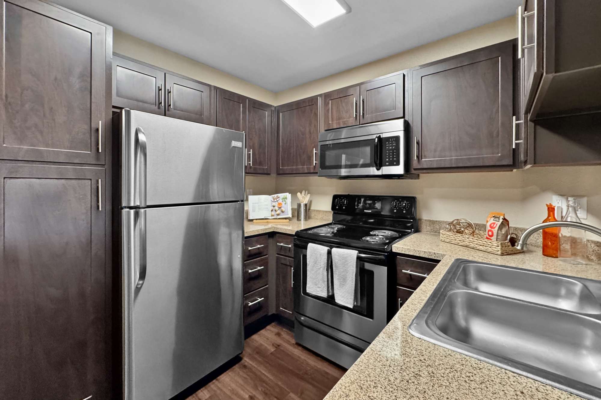 Renovated kitchen with brown cabinets and stainless steel appliances at Tuscany Village Apartments in Ontario, California