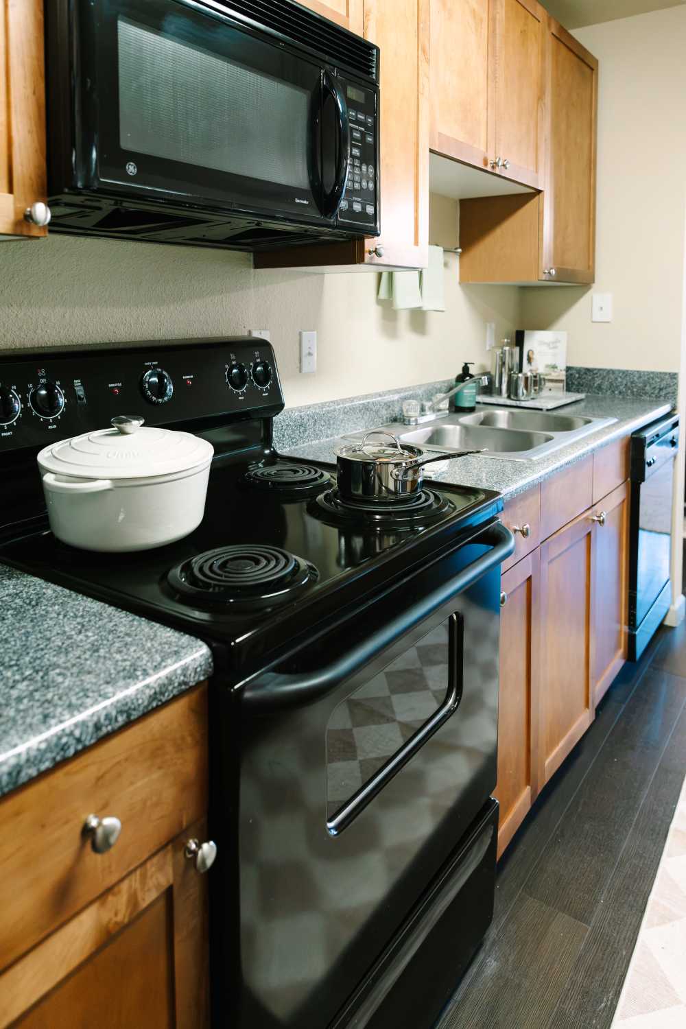Apartment kitchen featuring black appliances, wood cabinetry, solid-surface countertops, and double-basin sink at The Holly in Lubbock, Texas.