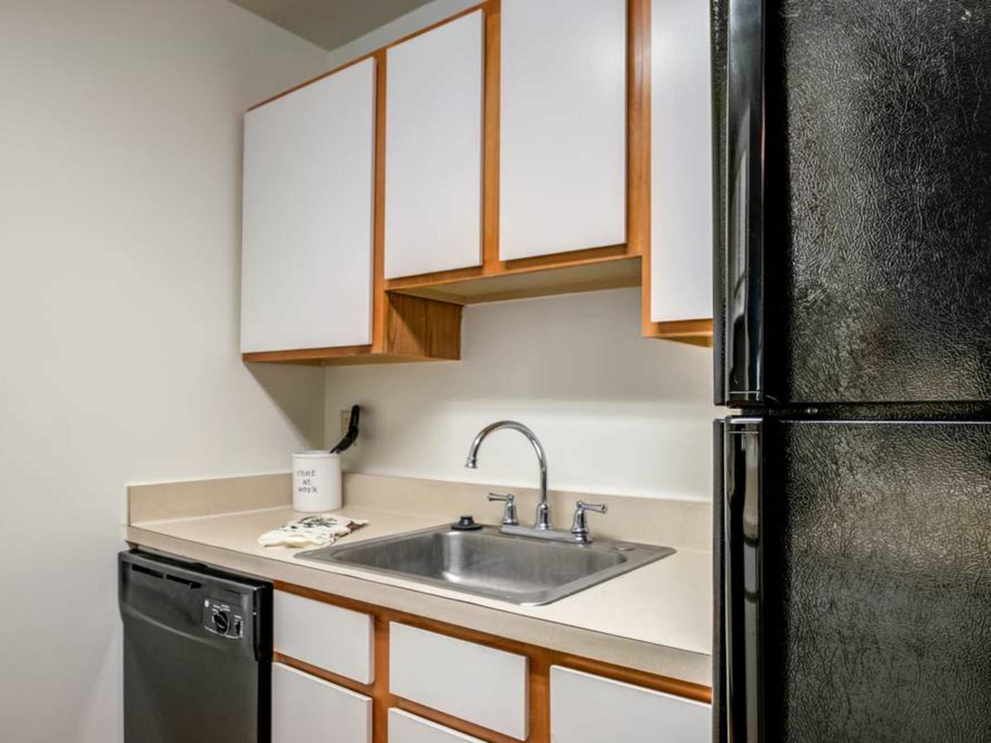 Compact kitchen with black appliances, wood cabinetry, and a stainless steel sink at The Vinings at Christiana Apartments in Newark, Delaware