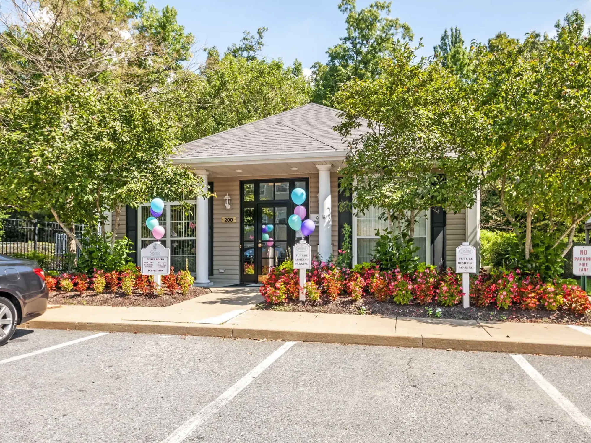 Welcoming leasing office entrance with colorful balloons and vibrant flower beds at The Vinings at Christiana Apartments in Newark, Delaware