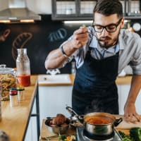 Man tasting sauce while cooking at One India Street Apartments in Boston, Massachusetts