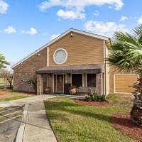 Two-story apartment building with stone accents, landscaped yard, and palm trees under a blue sky at Towne East Village Apartment Homes in Converse, Texas