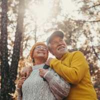 Elderly couple smiling together in a sunlit forest setting near Dr. Louis A. Venson Senior Lofts in Pittsburgh, Pennsylvania