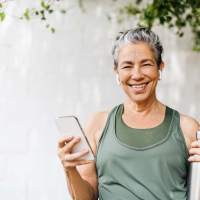 Smiling woman in workout attire holding phone outdoors near Dr. Louis A. Venson Senior Lofts in Pittsburgh, Pennsylvania