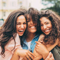 Three women laughing together outdoors, bright sunlight near Terramonte Apartment Homes in Pomona, California