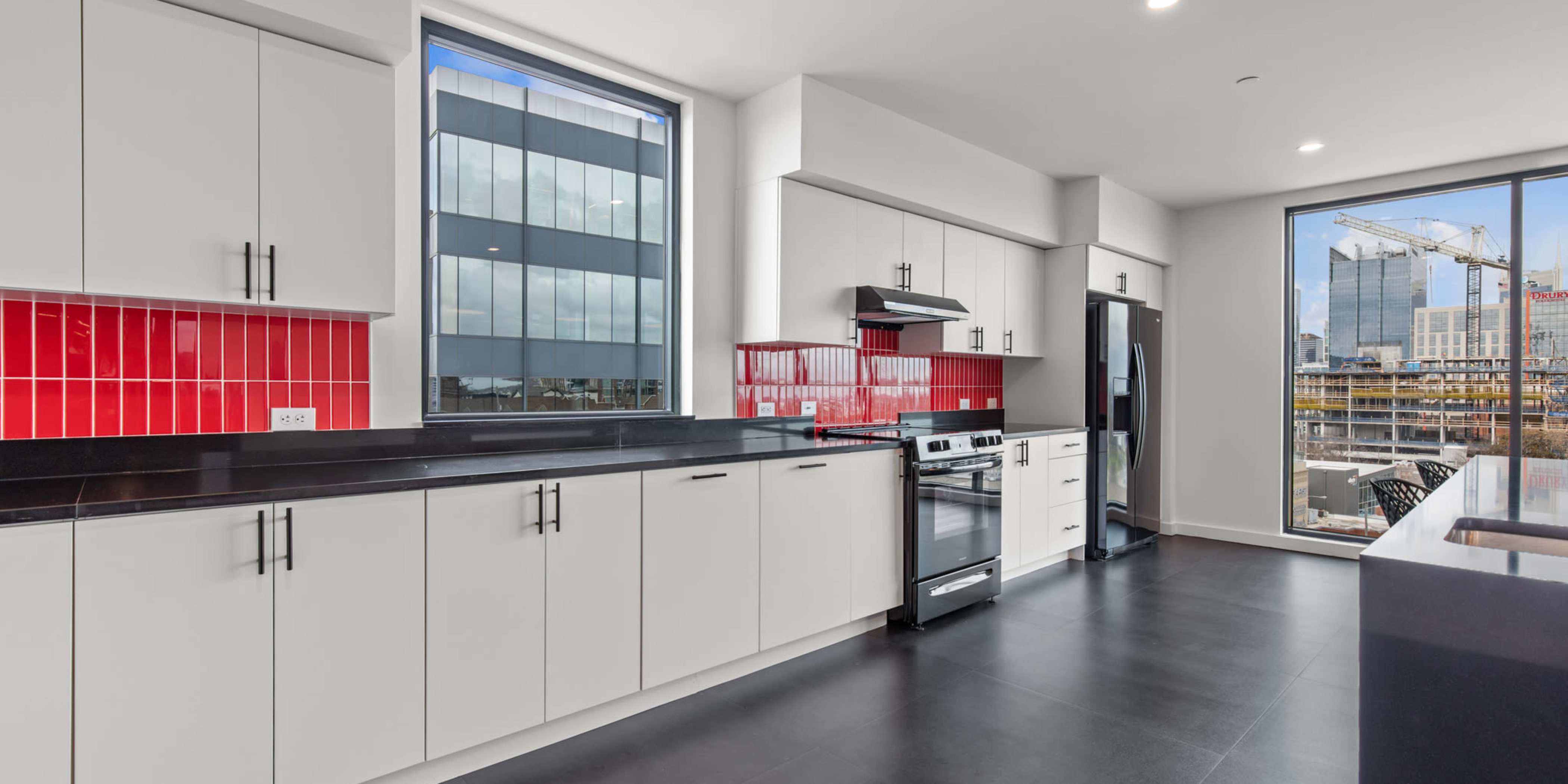 Apartments by Rutledge Hill, TN - Rutledge Flats - Community Kitchen with White Cabinets, Black Countertops, Red Tile Backsplash, Stainless Steel Appliances, and Large Windows