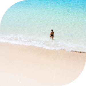 Aerial view of woman walking at the edge of a sandy beach at Romero Apartments in Pensacola, Florida