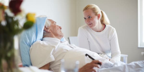 Caretaker sitting and talking with a resident laying in bed at Edgerton Care Center in Edgerton, Wisconsin