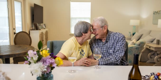 Residents couple sits at a dinning table, touching foreheads and holding hands at The Barclay at Boynton Beach in Boynton Beach, Florida