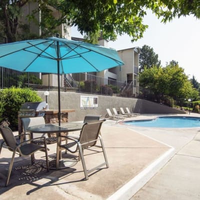 Table with chairs and an umbrella next to the refreshing pool on a nice sunny day at Sofi Belmar in Lakewood, Colorado