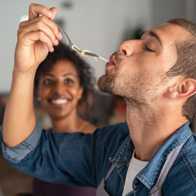 A man tasting food while a woman smiles in the background in their apartment at Thirty - One 32 Cypress in Hoover, Alabama