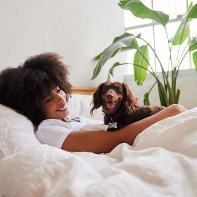 Woman lounging in bed with dog, surrounded by bright natural light and green plants at Valley Brook Townhomes in Rochester, New York