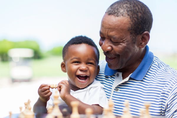Resident sitting at a game of chess with his young, smiling grandchild on his lap