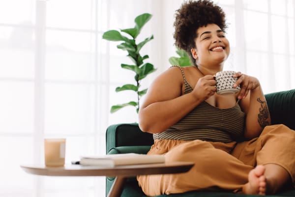 Resident smiling and drinking a cup of coffee in her living room at Cheltenham Station in Philadelphia, Pennsylvania