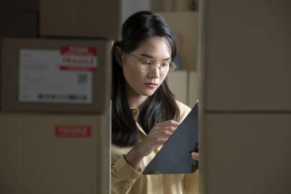 Woman in glasses checking clipboard among boxes