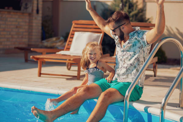 A father and his child smiling with their feet in the pool at Fairway View in Hialeah, Florida