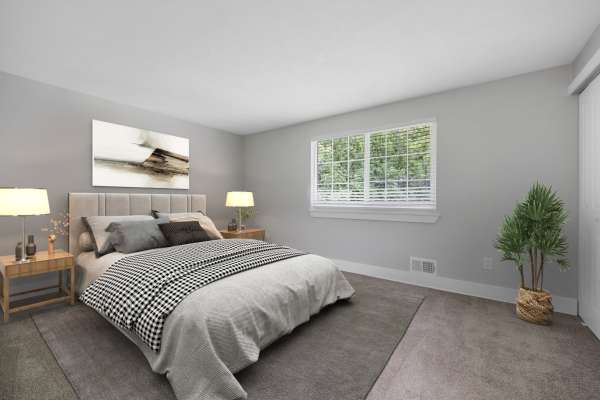 Bright bedroom with wood-style flooring, large windows, king bed, and cozy armchair at Valley Brook Townhomes in Rochester, New York