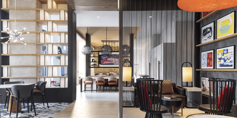 Resident lounge with seating areas and bookshelves looking into game room with television, pool table, and shuffle board at Solaire 8200 Dixon in Silver Spring, Maryland