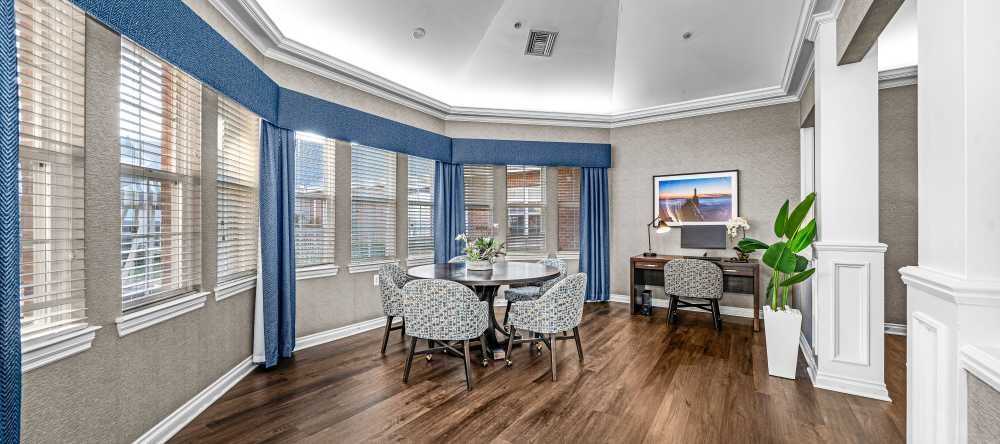 Sitting area with round table, blue curtains, large windows, and a desk with a computer