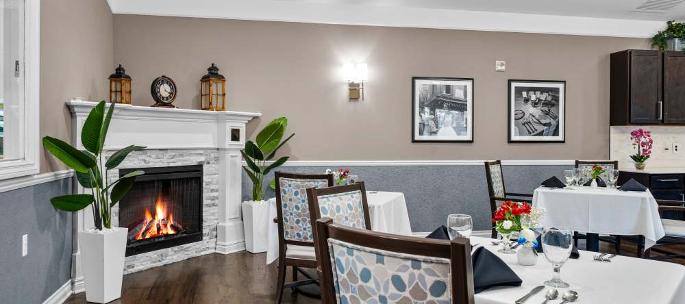 Dining room with a lit fireplace, patterned chairs, and tables set with place settings