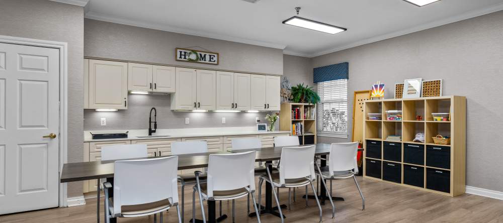 Activity room with long table, white chairs, cabinets, and shelves of books and supplies