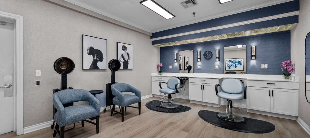 Bright salon with styling stations, blue chairs, large mirrors, and wall-mounted hair dryers