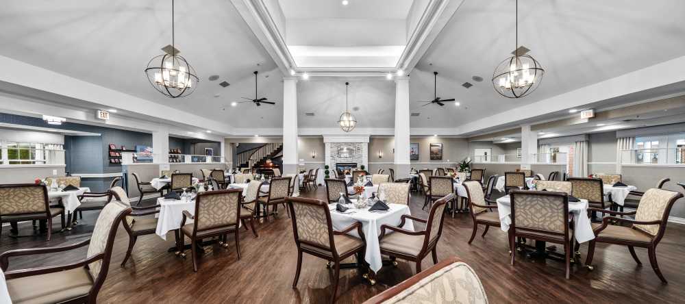 Large dining hall with white table settings and high ceilings at Waltonwood Cherry Hill in Canton