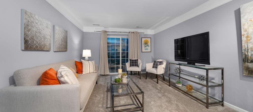 Bright living room with sofa, chairs, large window, and TV console at Waltonwood Cherry Hill in Canton