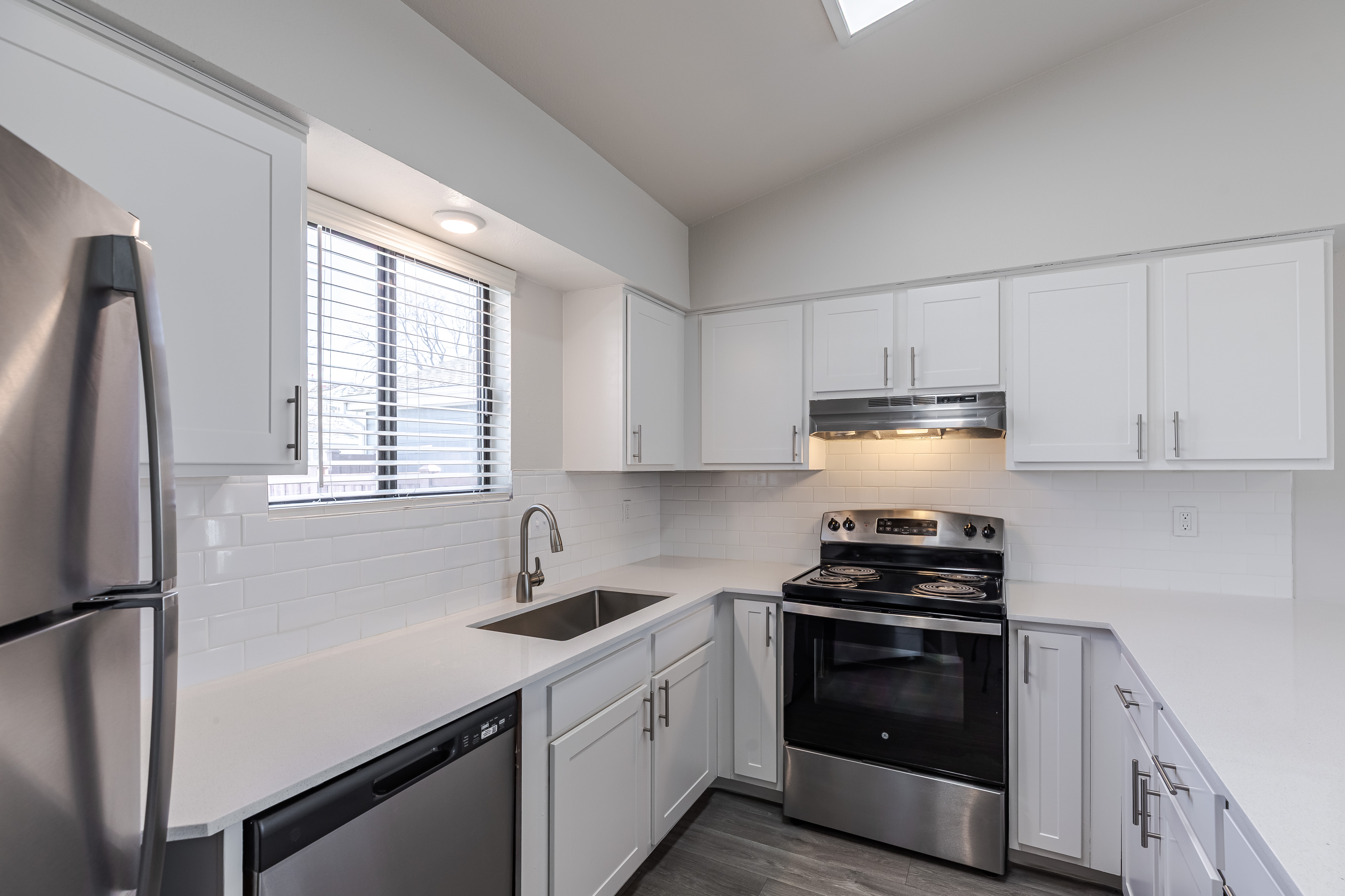 Upgraded kitchen with stainless steel appliances, white cabinets, stone counters, and wood-style flooring at Environs Residential Rental Community in Westminster, Colorado 