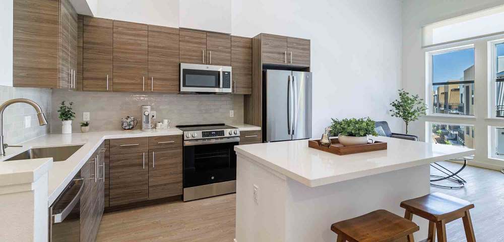 Bright modern kitchen featuring wooden cabinets, stainless steel appliances, and a countertop with bar stools at Sutter Green Apartments in Sacramento, California