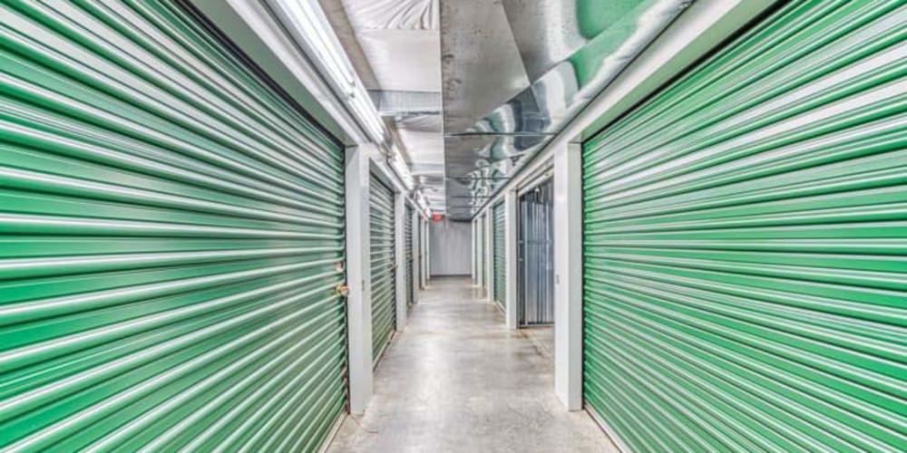 Clean and well-lit hallway along indoor storage units with bright green doors at Devon Self Storage in St. Louis, Missouri