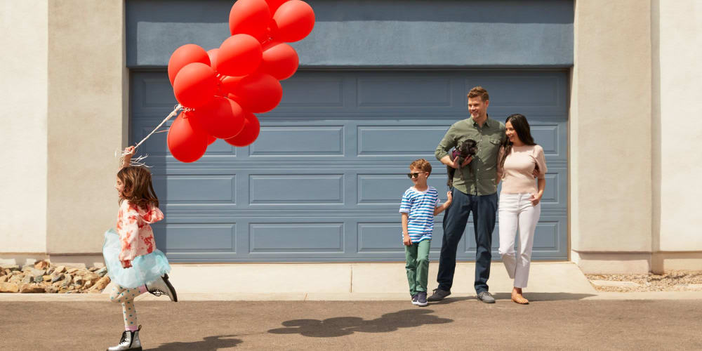 Young girl running with a bunch of red balloons while her family watches at BB Living at Light Farms in Celina, Texas