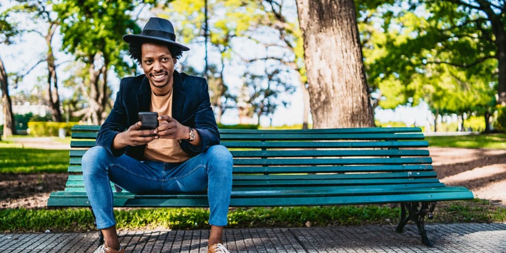 Resident looking at his phone on a park bench on a sunny day at Vista Creek Apartments in Castro Valley, California