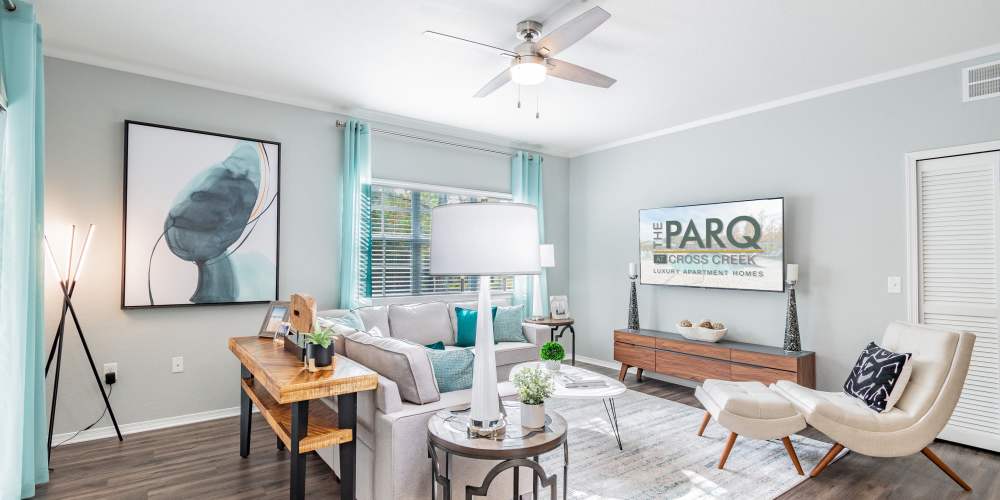 Furnished apartment living room with sectional sofa, ceiling fan, and large television at The Parq at Cross Creek in Tampa, Florida