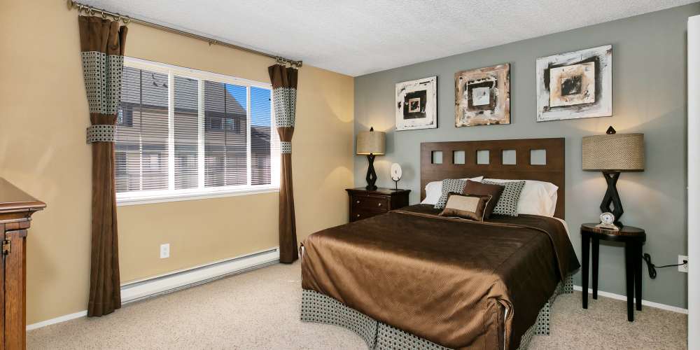 Model apartment bedroom with a large central bed and curtained window at Collins Junction in Lynnwood, Washington