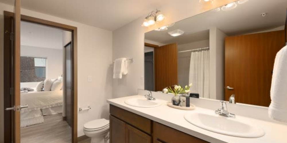 Apartment bathroom with a double sink and wide mirror at Four Pines Apartments in Burlington, Washington