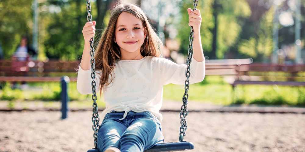 Happy smiling girl kid swinging on a swing near 353 Main Street Family Apartments in Redwood City, California